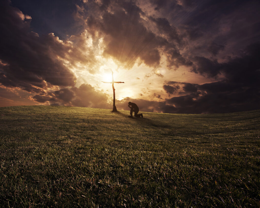 a man kneeling at a cross at sunset rXUS30WlR