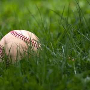 one aged and worn hardball or baseball laying in the green grass BYMUpwArs