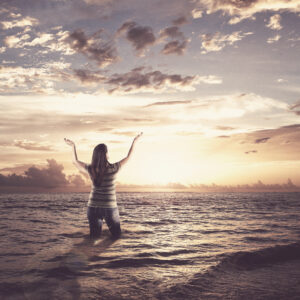 woman standing in the ocean and lifting her arms up in praise SXdjqCWlC