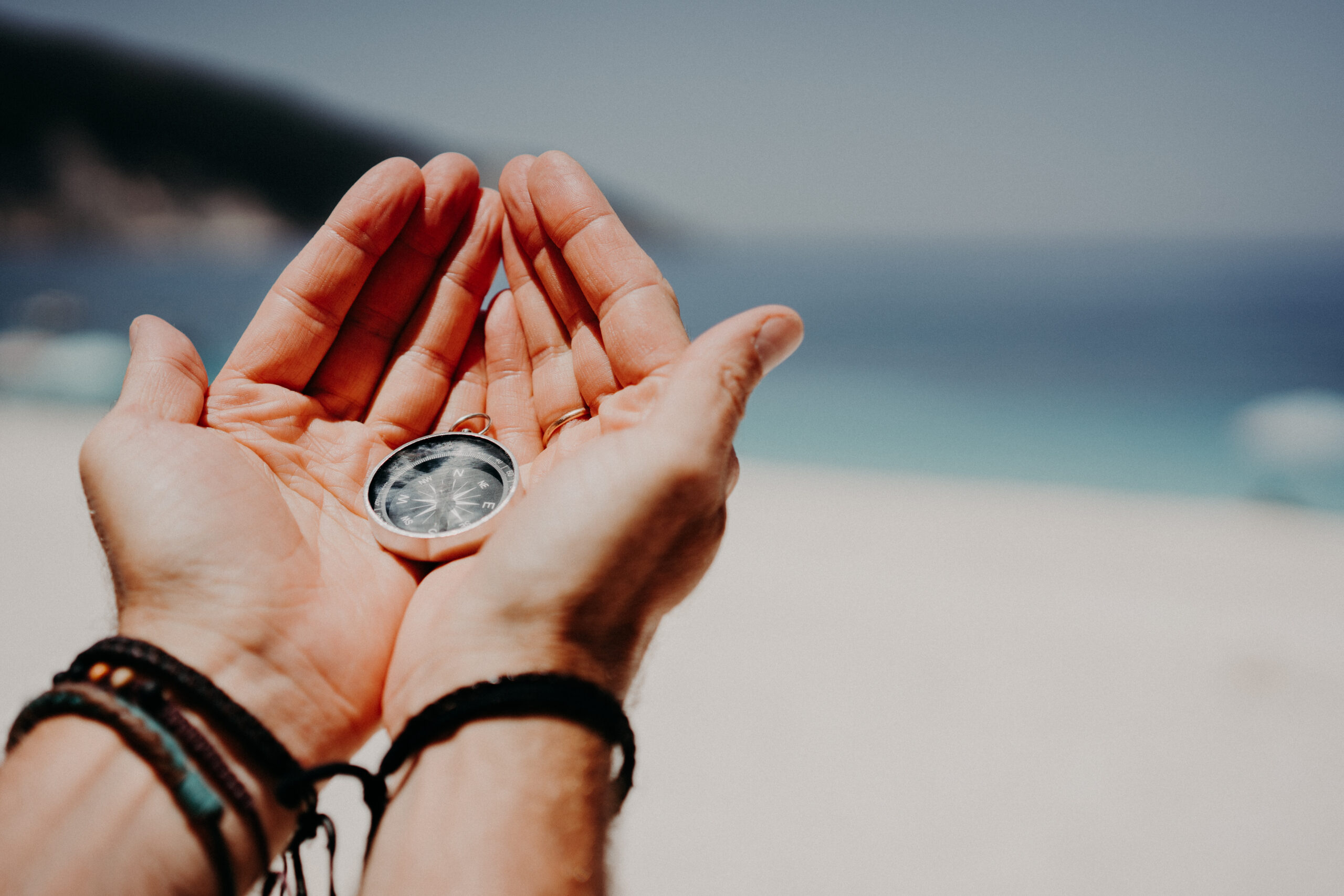storyblocks mans hand holding compass against the backdrop of beach and sea the concept of travel summer vacation holiday and journey BHMpPQhp14 scaled