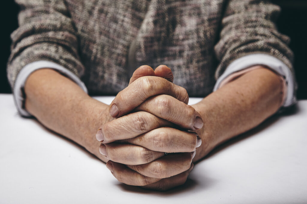 studio photography of praying hands of a senior woman on table old hands clasped on a table Hpl8MwLNYe