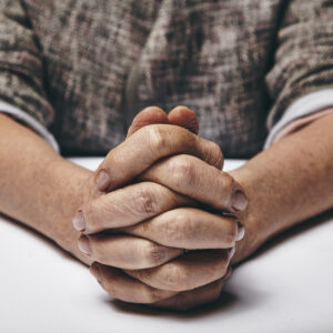 studio photography of praying hands of a senior woman on table old hands clasped on a table Hpl8MwLNYe