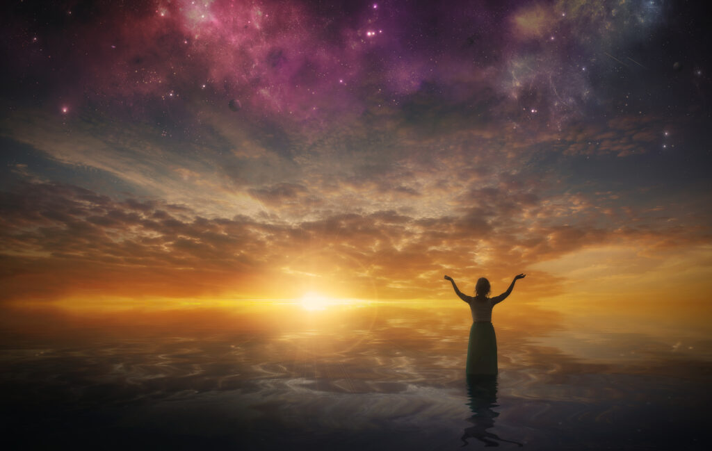 a woman lifts her arms in praise as the sun sets HXMWb1fx0