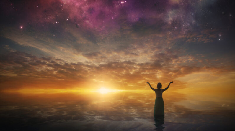 a woman lifts her arms in praise as the sun sets HXMWb1fx0