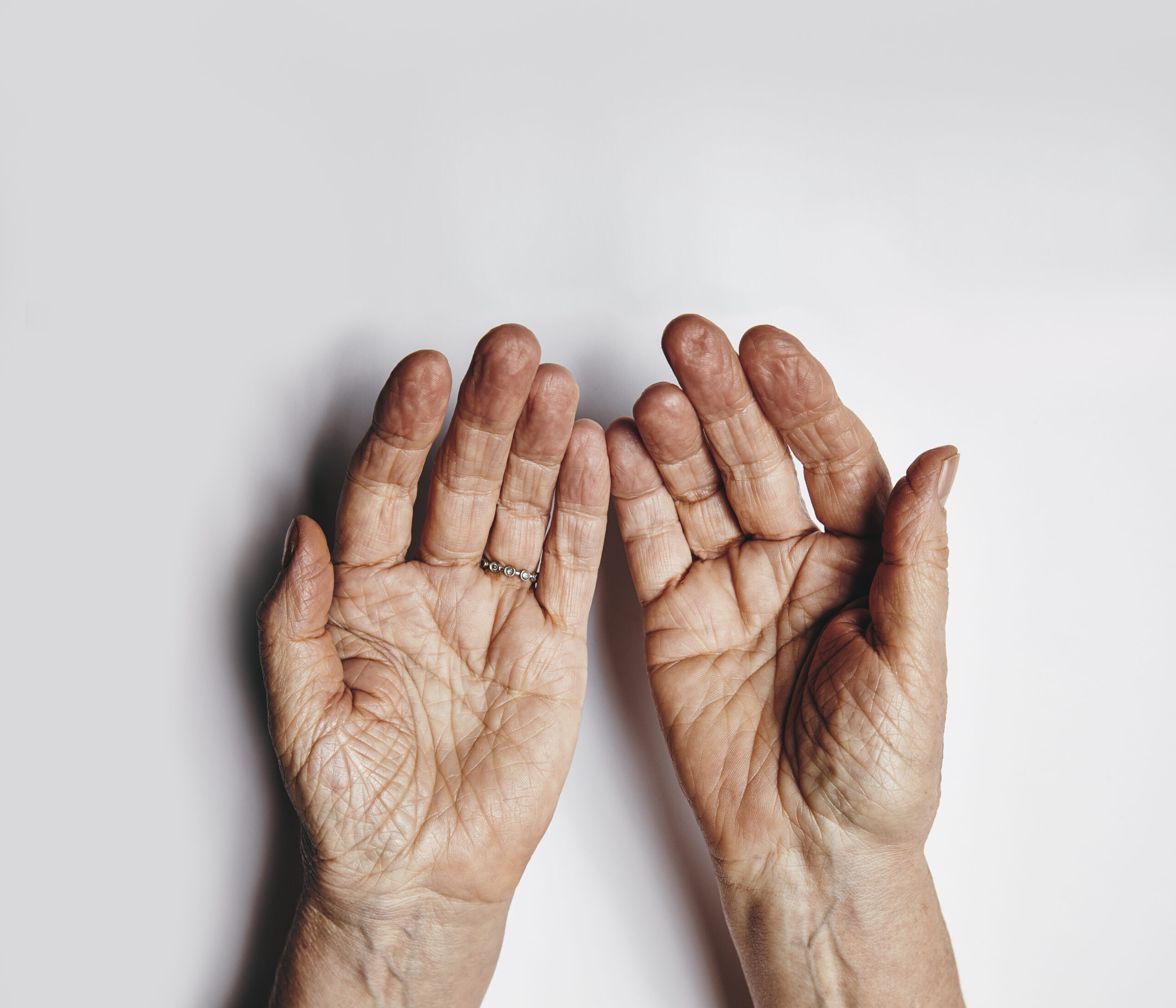 top view of two empty female hands over grey background senior woman hands pleading wrinkled palms of aged woman with copy space STW ePUEKx scaled