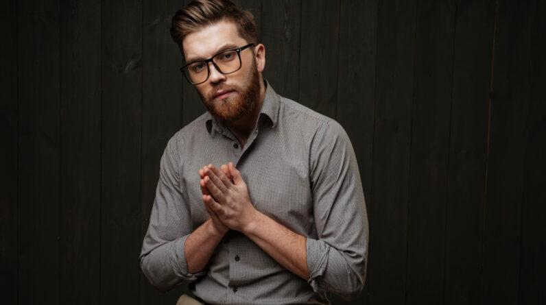 graphicstock portrait of a young bearded man in eyeglasses sitting and praying isolated on a black wooden background BLrmRuQOhx
